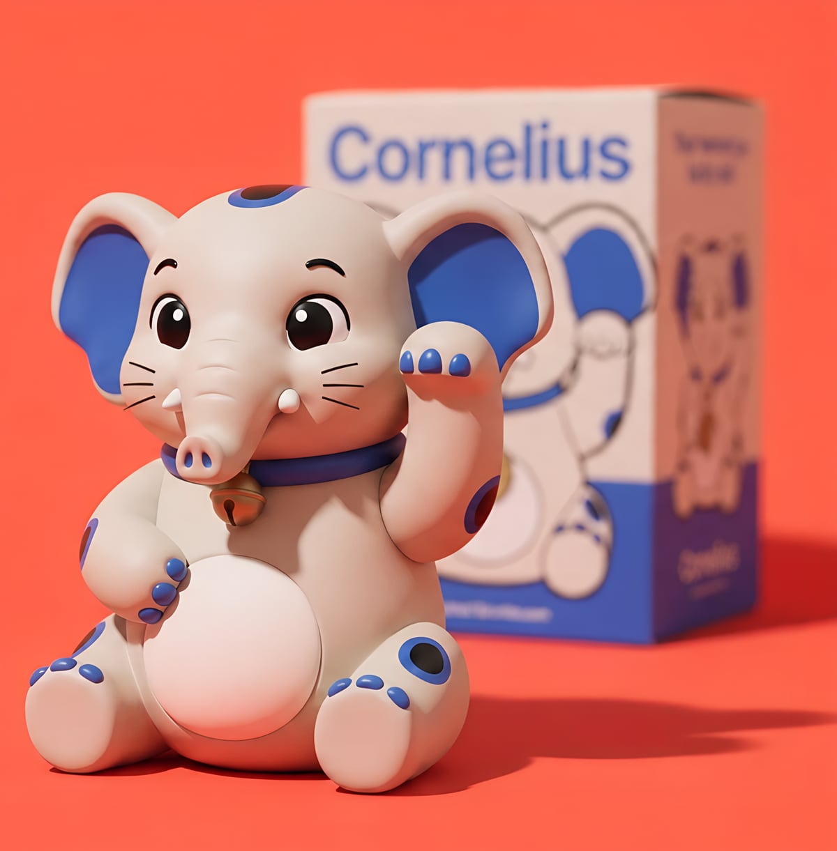 Cornelius, a bone-white vinyl elephant figurine with cobalt ears and a gold bell, waving like a lucky cat in front of its box